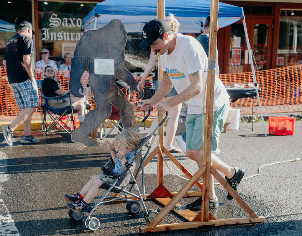 Oakridge Oregon Keg & Cask Festival: man pushing child on baby stroller under summer fair mist